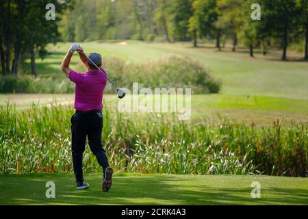 Rückansicht des männlichen Golfers mittleren Alters, der auf sonnigem Golf fährt Kurs Stockfoto