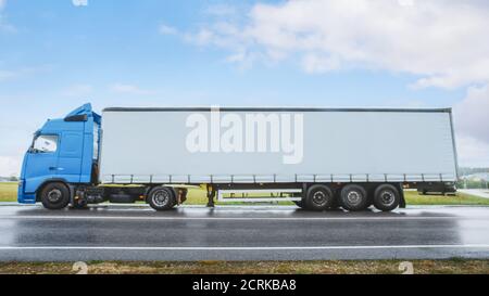 Seitenansicht Aufnahme eines blauen Langstrecken-Semi-Trucks mit angehängtem Lastenauflieger, der auf einer Straße im ländlichen Raum angehalten wurde. Logistik-Unternehmen Bewegt Waren Über Stockfoto