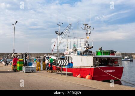 Fischer entladen ein Fischerboot am Hafen. Männer tragen Arbeitsuniform, gelbe wasserdichte Hose und Plastikstiefel. Fisch wird im Eis in p gehalten Stockfoto