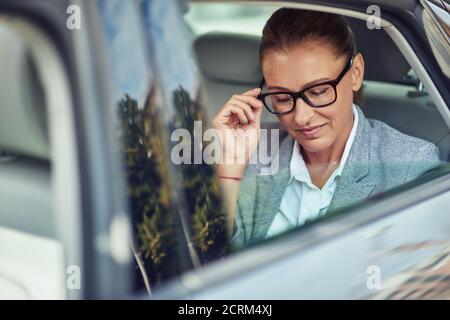 Schöne Geschäftsfrau mittleren Alters, die ihre Brille beim Sitzen justiert Auf dem Rücksitz im Taxi Stockfoto