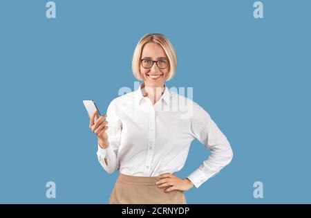 Portrait der Unternehmerin mit Handy arbeiten online oder Chat mit dem Client auf blauem Studio-Hintergrund Stockfoto