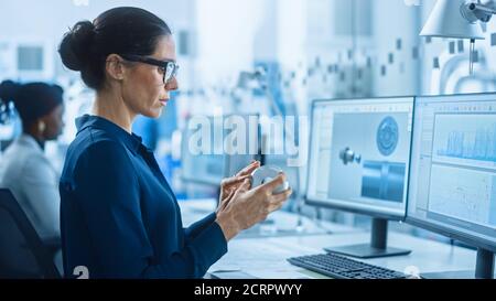 Ingenieurin, die am Personal Computer arbeitet, das Modell der industriellen Maschinerie Mechanismus inspiziert. Sie arbeitet mit Team of Industrial Professionals in Stockfoto