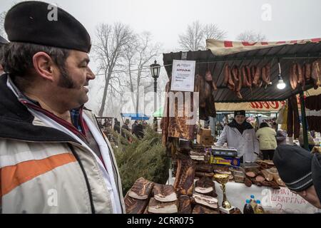 KACAREVO, SERBIEN - 18. FEBRUAR 2017: Mann, Vater, der seinen Sohn, einen Jungen, einen zukünftigen Metzger, auf einem Stand ansieht, der serbisches Wurstfleisch verkauft Stockfoto