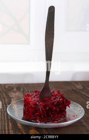 Vegetarischer Salat aus Rüben, Karotten, Knoblauch und Olivenöl auf einem Teller ist auf dem Tisch, in ihn gesteckt Stockfoto