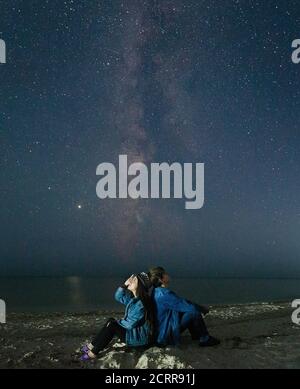 Ein verliebter Pärchen sitzt am Strand und beobachtet den nächtlichen Sternenhimmel. Stockfoto