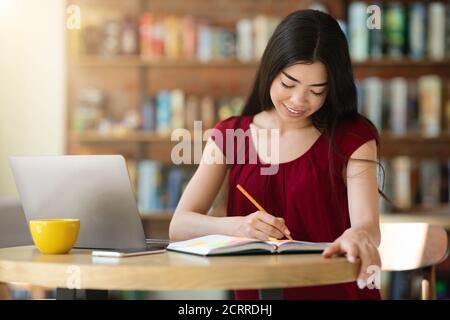 Planung Des Arbeitsplanes. Asiatische Freiberufliche Frau Nimmt Notizen Zu Notizblock Im Café Stockfoto