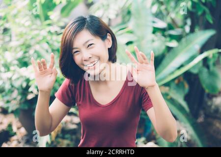 Schönes Porträt junge asiatische Frau lächelnd winkende Hand im Garten zu Hause, freundliches Mädchen und Ausdruck positive Emotion, Hallo und Gruß, ein Stockfoto