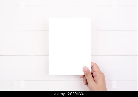 Hand des jungen Mannes mit Plakat oder Karte oder Broschüre mit weißem Papier leer auf Holztisch, Grußkarte, a5, a4, Flyer Werbung und Nachricht für Stockfoto