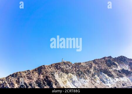 Klippe und Leuchtturm auf der südlichen Insel Thira auf griechischen Inseln an einem klaren, sonnigen Tag mit hellem, blauem Himmel. Akrotiri, Santorini, Griechenland. Akroti Stockfoto