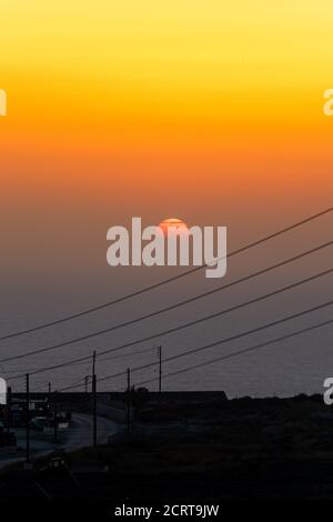 Sonnenuntergang über dem Meer und der Stadt. Orangefarbener und gelber Himmel mit roter Sonne. Stromkabel im Vordergrund. Hochformat Stockfoto