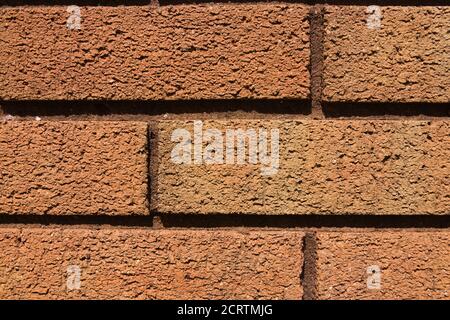 3 - Makro-Nahaufnahme der goldorangefarbenen Ziegelwand. Durch warmes natürliches Sonnenlicht beleuchtet. Düstere und klumpige abstrakte Hintergrundtextur. Mauerwerk Ziegelsteinlegung. Stockfoto