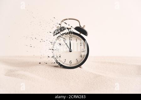 Konzept des Vergehens, die Uhr zerfällt in Stücke. Analoge Uhr im Sand, mit Dispersionseffekt. Stockfoto