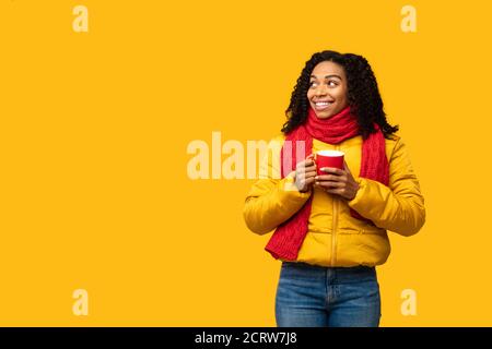 Schwarze Frau Trägt Winterjacke Halten Kaffee Becher, Gelber Hintergrund Stockfoto