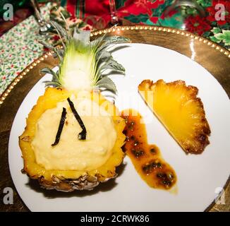 Eis und zwei Vanilleschoten in einer halben Ananas. Und eine Scheibe geröstete und karamellisierte Ananas. Platziert auf einem weißen und einem goldenen Teller. Stockfoto