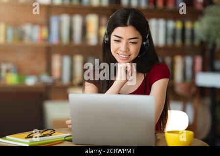 Fröhliche Koreanische Dame Im Headset Beobachten Webinar Über Laptop In Café Stockfoto