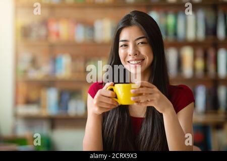 Teezeit. Lächelnde Asiatische Frau Mit Becher Mit Heißem Getränk Im Café Stockfoto