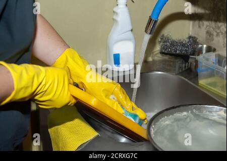 Geschirr unter fließendem Wasser aus der Nähe waschen. Damenhänden in gelben Haushaltshandschuhen reinigen Geschirr vor dem Waschen in der Spülmaschine Stockfoto