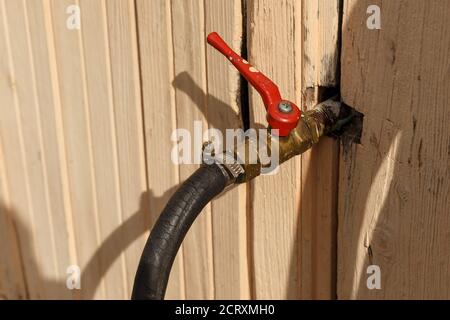 Der Wasserhahn ragt aus der Wand des Hauses. Bügeleisen Wasserhahn mit einem roten Griff. Stockfoto