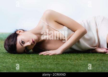 Junge Frau im Seidenkleid auf grünem Gras liegend Weiß Stockfoto