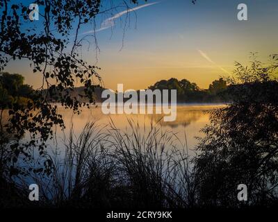 Nach Sonnenaufgang erheben sich Nebelschwaden über dem See Stockfoto