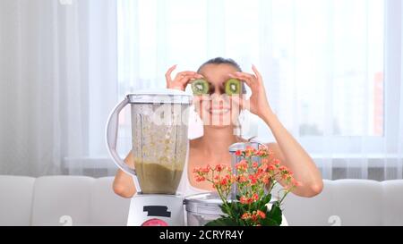 Glückliche junge Frau bereitet leckere nahrhafte Smoothie im Mixer. Lustige Frau macht Augen aus Kiwi. Stockfoto