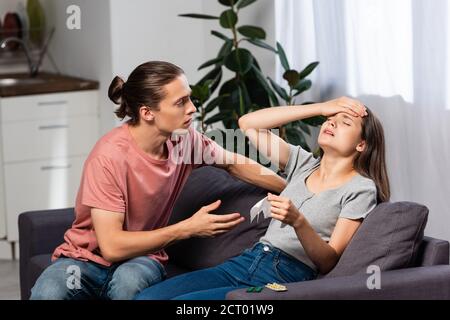 Besorgt Mann sitzt neben kranken Freundin berühren Stirn während leiden Von Kopfschmerzen Stockfoto