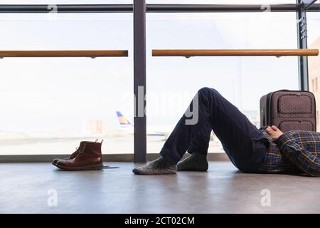 Männlicher Reisender, der sich auf dem Boden in der Nähe des Fensters ausruhte, während er darauf wartete Flug am Flughafen Stockfoto