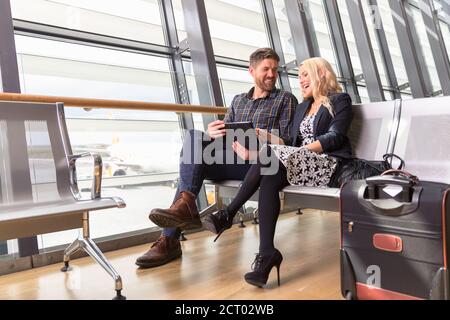 Positive Mann und Frau sitzen auf der Bank und browsing Tablet Am Flughafen Stockfoto