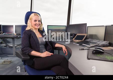 Weibliche Flugoperationsoffizier lächelnd für Kamera auf Stuhl in Büro am Flughafen Stockfoto