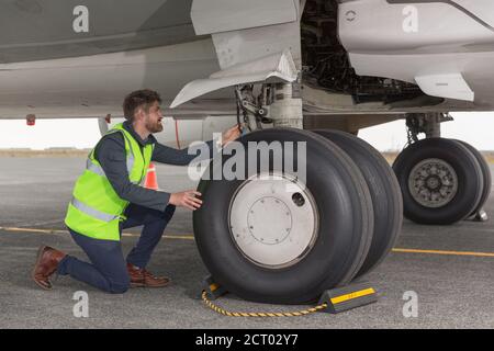 Mann in der Weste untersucht Schnüre auf Rädern des Flugzeugs, während Arbeiten am Flughafen Stockfoto