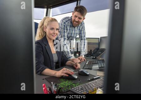 Mann, der mit einer Kollegin im Dispatcher-Büro am Computer spricht Am Flughafen Stockfoto