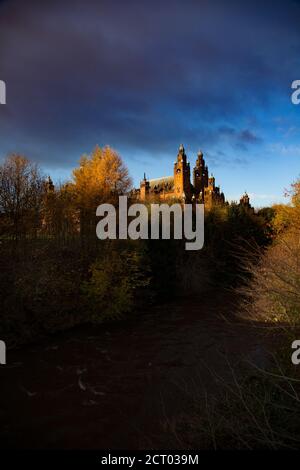 Glasgow / Schottland - 13. Nov 2013: Blick auf die Kelvingrove Art Gallery und das Museum durch den Kelvin Fluss und die Bäume. Abendlicht mit orangefarbenem Sonnenuntergang. Stockfoto