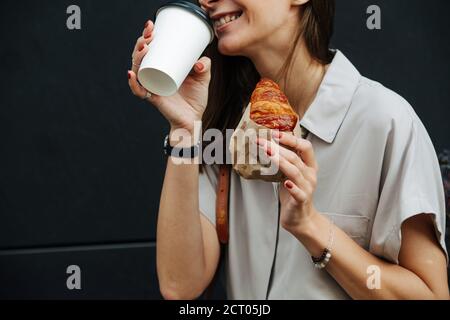 Lächelnde Frau auf der Straße trinkt Kaffee mit Croissant, abgeschnitten Stockfoto