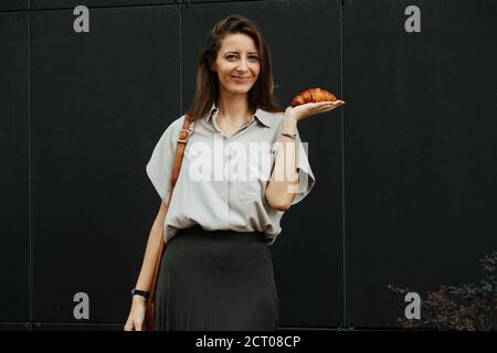 Glücklich lächelnde Frau hält knackig frisch gebackene Croissant auf sie Handfläche Stockfoto