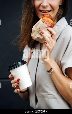 Frau auf der Straße posiert in Croissant und Kaffee in den Händen, abgeschnitten Stockfoto