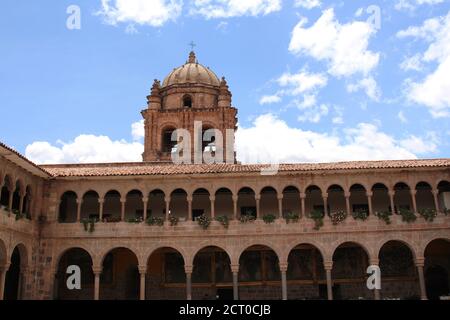 Der Glockenturm auf einer zweistöckigen Steinmauer, die mit Säulen und Bögen gesäumt und mit Blumen und Kunstwerken gefüllt ist, im Belmond Monasterio Hotel in Cusco, Stockfoto