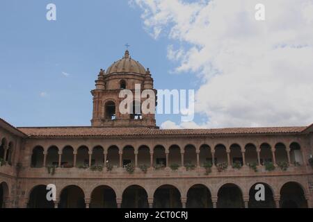 Ein Glockenturm auf einer zweistöckigen Steinmauer, die mit Säulen und Bögen gesäumt und mit Blumen und Kunstwerken gefüllt ist, befindet sich im Belmond Monasterio Hotel in Cusco, P Stockfoto