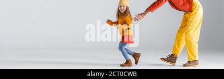 Teilansicht von Mutter und Tochter in bunten roten und gelben Outfits läuft auf grauem Hintergrund, Panoramaaufnahme Stockfoto