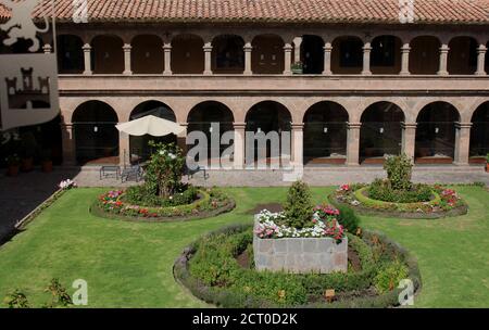 Ein Innenhof mit drei Blumengärten, umgeben von zweistöckigen Steinmauern, gesäumt von Säulen und Bögen, im Belmond Monasterio Hotel in Cusco, per Stockfoto