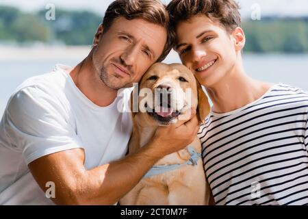 Vater und Sohn schauten auf die Kamera und umarmten Golden Retriever Stockfoto