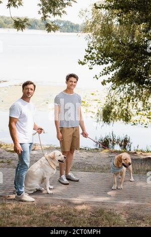Vater und Sohn halten Leine, während sie mit goldenen Retriever stehen In der Nähe des Sees Stockfoto