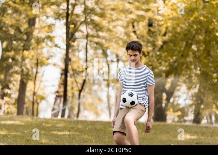 Teenager Junge spielt Fußball in der Nähe von Bäumen im Park Stockfoto