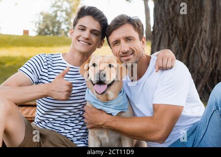 Teenager Sohn zeigt Daumen nach oben und umarmt Vater in der Nähe golden abrufen Stockfoto