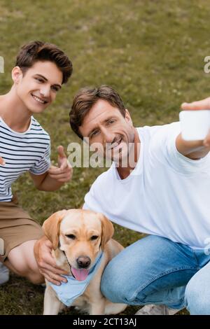 Selektiver Fokus des Teenagers Junge zeigt mit dem Finger auf golden retriever während Vater Selfie Stockfoto