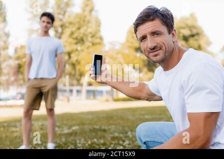Selektiver Fokus des Vaters hält Smartphone mit leerem Bildschirm in der Nähe Teenager Sohn im Park Stockfoto