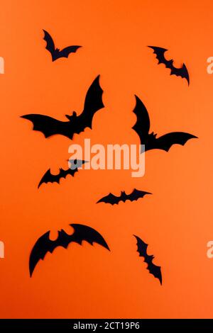 Wenige verschiedene Silhouetten von fliegenden schwarzen Fledermäusen auf hellorangefarbenem Papierhintergrund. Silhouetten sind handgeschnitzt aus Pappe. Flach legen mit Halloween Stockfoto