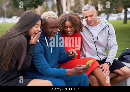 Multi ethnische Freunde im Freien suchen Smartphone-Bildschirm. Diverse Gruppe Menschen Afro american asiatisch kaukasisch verbringen Zeit zusammen multirassischen männlichen Fem Stockfoto