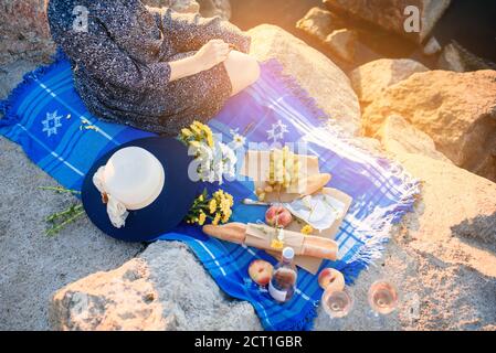 Ein Mädchen mit Blumen am Meer in der Morgendämmerung bei einem Picknick. Romantischer Morgen.Sommer - Mädchen mit einem Korb geht auf ein Picknick Stockfoto