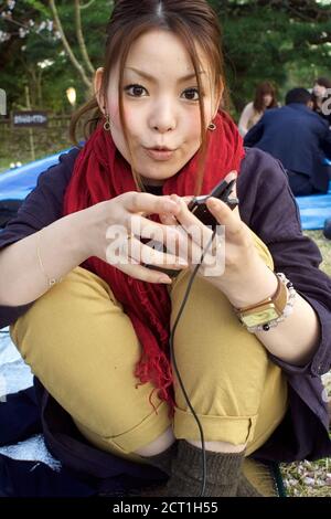 Japanische Mädchen mit Musikspieler und trendigen Uhr bei einem Picknick in Ritsurin koen Garten, Takamatsu Stadt, Shikoku, Japan 2012 Stockfoto