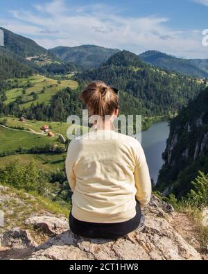 Junges Mädchen in der Natur. Rückansicht Porträt einer alleinerziehenden Frau, die den Spajici See aus der Höhe in Westserbien beobachtet Stockfoto